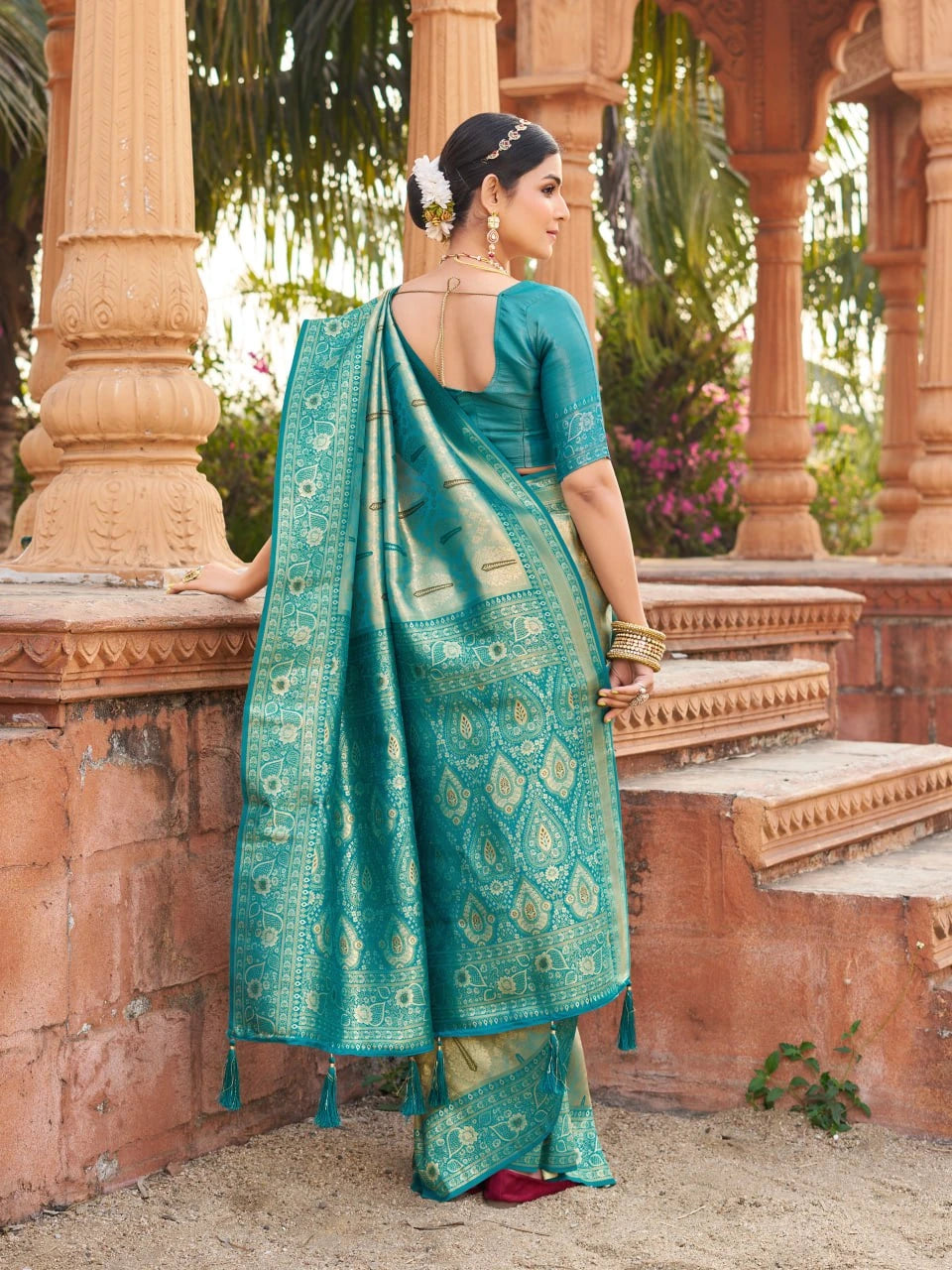 Woman in a teal saree standing in front of an architectural structure with columns.